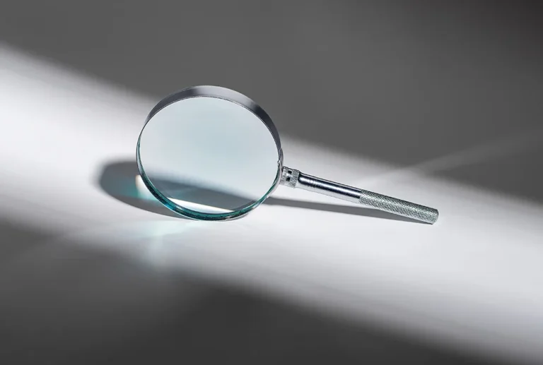 Silver magnifying glass on a bright surface with a long diagonal shadow. If used as a search cue, represents the action 'Search'.