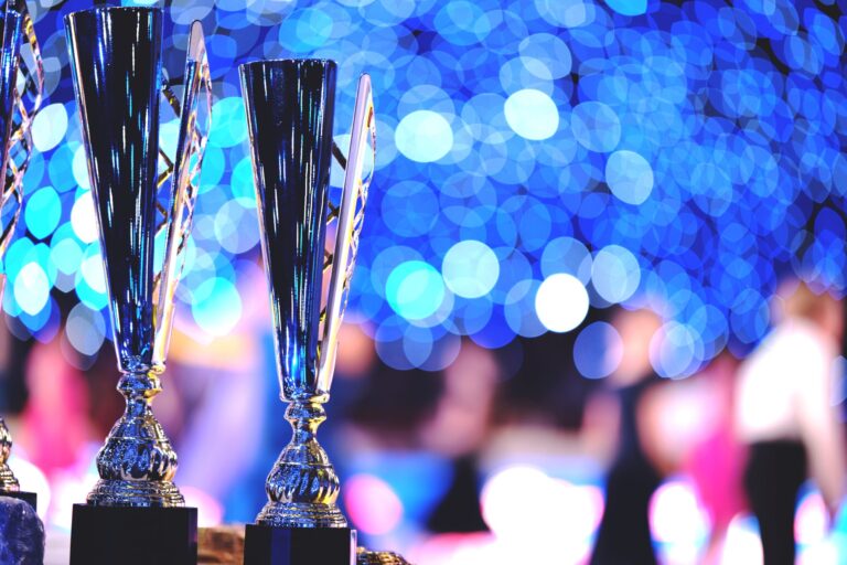 Close-up of silver trophies on black bases at a celebration, with blue bokeh lights in the background.